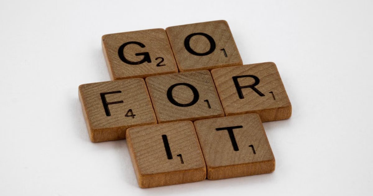 Close-up of Scrabble letters forming the phrase 'Go For It' on a white background.