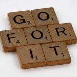 Close-up of Scrabble letters forming the phrase 'Go For It' on a white background.