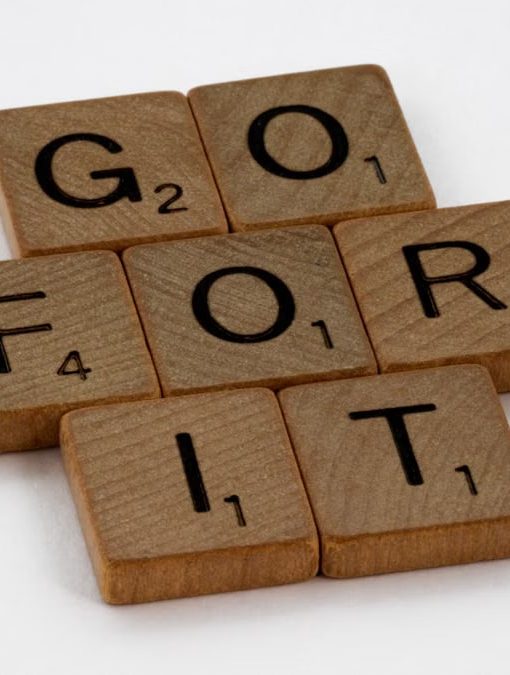 Close-up of Scrabble letters forming the phrase 'Go For It' on a white background.