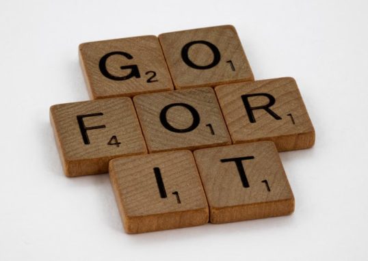 Close-up of Scrabble letters forming the phrase 'Go For It' on a white background.